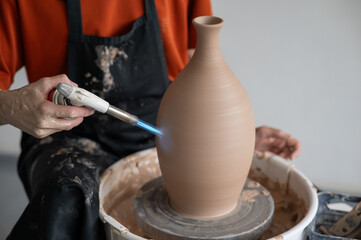 Close-up of a potter's hands firing a jug with a gas burner on a potter's wheel.