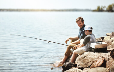 Happy father, son and learning with fishing rod on rock by lake, ocean or beach together in nature....