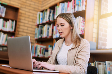 Fototapeta premium Research, typing and woman in library with laptop, education and exam preparation at university. Female student, technology and studying at table for knowledge, communication and learning on internet