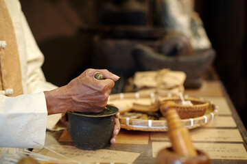 Close-up of old man grinding herbs in bowl in traditional Asian apothecary