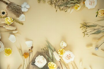 A beige background is bordered by an arrangement of various dried and fresh flowers, including white and pale yellow roses, cotton flowers and various dried grasses and leaves. 