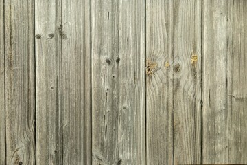 A closeup of a wooden floor with planks. The wood looks aged and weathered and has various shades of brown and natural grains. The surface has a slightly rough texture with visible lines and spots.