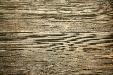 A closeup of a wooden floor with planks. The wood looks aged and weathered and has various shades of brown and natural grains. The surface has a slightly rough texture with visible lines and spots.