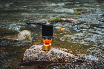 A stove is placed on a large rock in the middle of a fastflowing watercourse, surrounded by grass...
