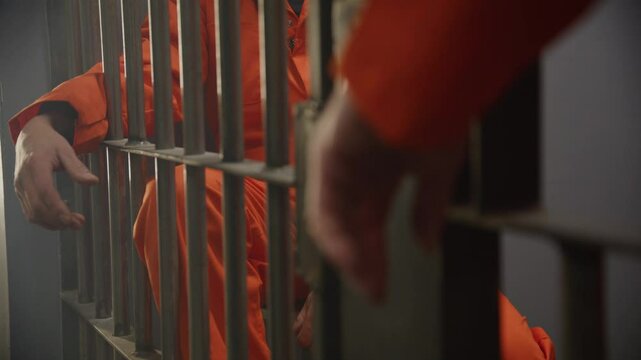 Zoom out from hands in crowded prison cell block