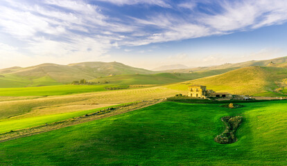 countryside sunset in green hills of spring fields with old castle farm and mountains on background of evening landscape