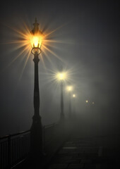 Foggy night scene with glowing street lights casting a mysterious and quiet ambiance. Suitable for surreal, urban, or atmospheric backgrounds.