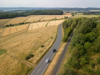 An aerial view of a rural landscape with fields and a winding road with cars driving through.