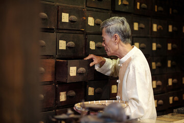 Senior apothecary choosing ingredients from drawer in drug store