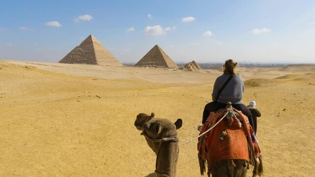 Woman on camel rides off in distance with guide to Great Pyramids of Giza
