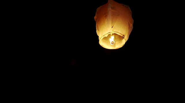 lose-up view of a single sky lantern glowing brightly against a dark night sky