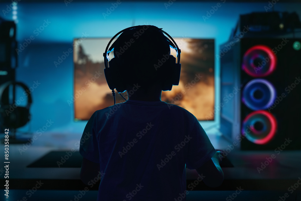 Poster low-light, high-contrast image of a boy playing a computer game on a gaming pc, viewed from behind, 