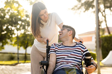 An adult man with a disability sits in an automatic wheelchair with a young woman in a park at...