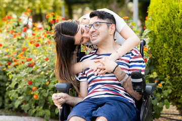 An adult man with a disability sits in an automatic wheelchair with a young woman in a park at...