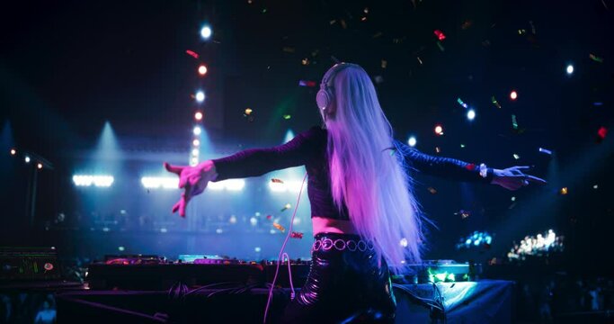 Girl Performing at a DJ Concert Live on Stage with Falling Confetti. Talented Music Producer Dancing, Mixing Energetic Dance Hits on Turntables. Young Female Engaging with the Crowd. Back View Footage