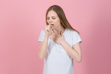 Attractive caucasian young woman blonde in casual white t-shirt covers mouth with her hand and suffers from coughing isolated on pink studio background. Virus, bronchitis, asthma.