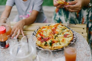 A casual outdoor scene with a child reaching for a drink and an adult holding a pizza slice, ideal for summer gatherings or family-friendly events.