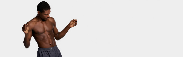 Fototapeta premium An African American man stands shirtless against a pure white backdrop, showcasing a beauty routine.