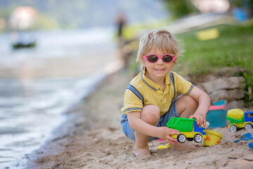 Little toddler child, cute boy, playing with toys in the sand on a lake