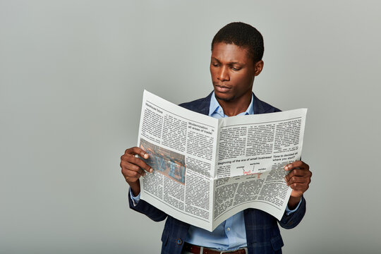 Stylish African American businessman in checkered blazer, fully immersed in reading a classic newspaper.