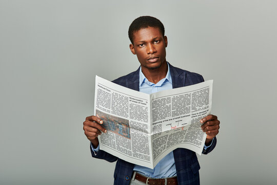 African American man in checkered blazer reading a newspaper on a grey background.
