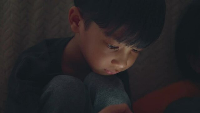 Asian boy is sitting using mobile phone in dark room and light comes from his mobile phone. internet, smart Phone addiction concept