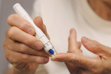 혈당 측정을 하고 있는 여성 어르신의 손 클로즈업. 당뇨병 관리 개념