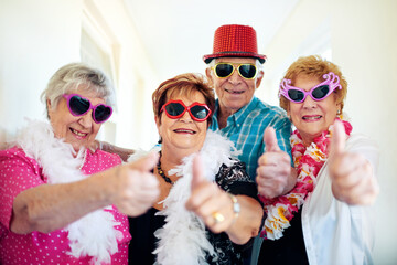 Thumbs up, smile and sunglasses with senior friends in hallway of retirement home for goofy party on weekend. Portrait, funny and eyewear with happy mature people having fun in elder care apartment