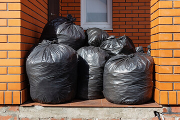 A pile of large black bags of garbage near the house. Full plastic bags filled and lying near the...
