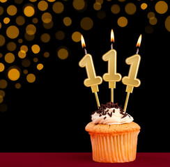 Birthday candle with cupcake - Number 111 on black background with out of focus lights
