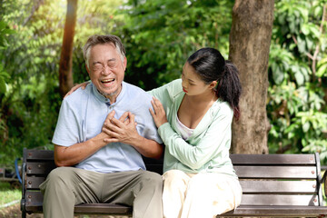 Fototapeta premium Elderly Asian man experiencing a heart attack during take a walk in park with daughter. Teenage girl help senior grandpa who has cardio problems chest pain while rest on bench in outdoors green garden