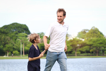 Father and son holding hands while walking in the park. Happy family, parent and kid spending time outdoors together in beautiful garden on holiday. little boy child playing with father outside.