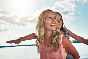 Playing, mother and child on beach with piggyback, smile and ocean on adventure holiday in...