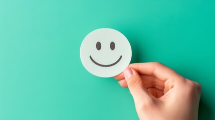 A Hand Holding a Round White Smiley Face Sticker with Black Eyes Against a Green Background.