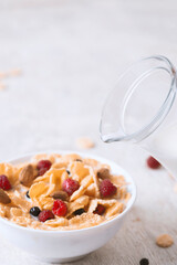bowl of corn granola with milk, fresh raspberries, blueberries .and a glass  on white wooden board for healthy breakfast,