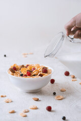 bowl of corn granola with milk, fresh raspberries, blueberries .and a glass  on white wooden board for healthy breakfast,