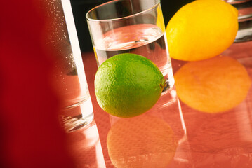 A glass of water stands on the table and green and yellow lemon.