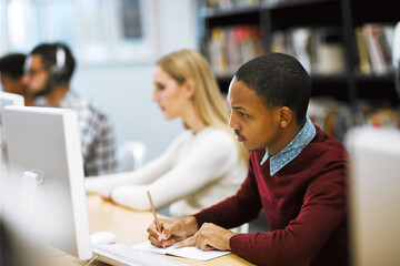 Writing, notes and college student at computer in library for university education, online course or project research. Reading, studying and man with notebook for web exam, elearning and planning.