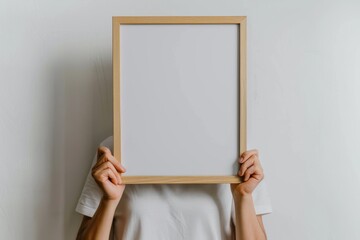 Person holding empty wooden frame against white wall background
