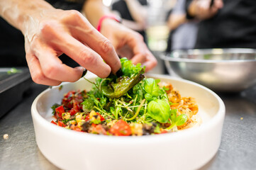 Close-up of a chef’s hands skillfully garnishing a vibrant salad with fresh green leaves in a white bowl