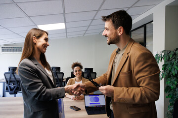 Happy mid aged business woman manager handshaking greeting client in office.