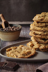 Chocolate chip cookies on table with chocolate and milk on dark brown background 