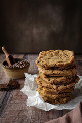Chocolate chip cookies on table with chocolate and milk on dark brown background 
