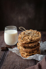 Chocolate chip cookies on table with chocolate and milk on dark brown background 