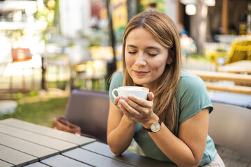 Stylish young woman drinking coffee at the cafe, looking away. Woman enjoying cappuccino in a cafe.