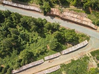 Aerial view of a forest area with stacks of cut logs along a road shaped like an arrow.