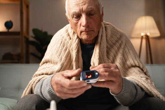 Senior man using pulse oximeter to check health at home, monitoring oxygen levels