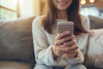 A happy young woman, sitting at home on the couch using her smartphone, smiling and looking at the screen while shopping online or working on social media apps. Social concepts, lifestyle