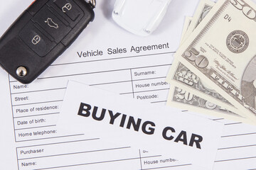 White toy car, car key, dollar banknotes and vehicle sales agreement. Inscription buying car....