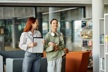 A redhead woman mentors a teenage girl in a library, after-school educational support.